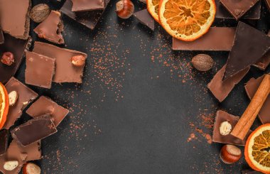 Koyu gıda arka planı çikolata parçaları, kakao tozu, fındık ve kurutulmuş portakal dilimleri metin, afiş veya reklam tasarımı için kopya alanı ile çerçeve oluşturur.