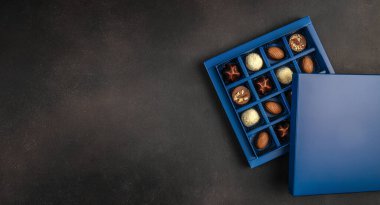 Fotokopi alanı olan koyu dokulu arka planda çeşitli pralinler ve trüf mantarları olan mavi, lüks çikolata hediye kutusu, birinci sınıf şekerleme reklamları, tatil kampanyaları ve lüks marka afişleri için ideal..