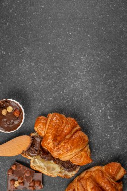 Kremalı çikolatalı fındık ezmeli gevrek kruvasan. Koyu taştan arka planda çikolata parçacıklarıyla servis ediliyor. Fotokopi alanı olan düz kompozisyon.