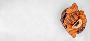 Çikolata dolgulu çeşitli altın kruvasanlar ve hasır sepette koyu çikolata parçaları, üzerinde fotokopi alanı olan üst manzara fırın afişi..