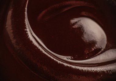 Erimiş koyu çikolatanın soyut kıvrımları parlak desenli ve zengin kakao rengi, makro gıda arka planı tatlı markası, ambalaj ve afiş tasarımı için ideal.