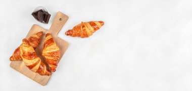 Taze pişmiş kruvasan, ahşap tahtada koyu çikolata parçaları, açık arkaplanda üst görünüm fırın kompozisyonu ve yemek reklamları için fotokopi alanı.