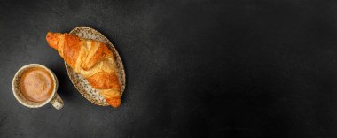 Seramik tabakta kruvasan, siyah arka planda kahve fincanı, fotokopi alanı olan basit kahvaltı kompozisyonu.