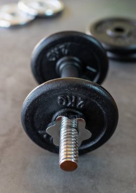 Beton yüzeyde 2 kg demir levhalar ve altta daha fazla ağırlık plakası olan Dumbbell.