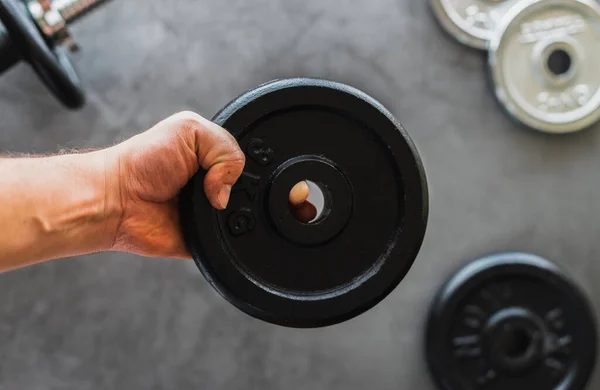 stock image White person's hand holding a 3g iron weight plate over a background with dumbbells and plates of different weights