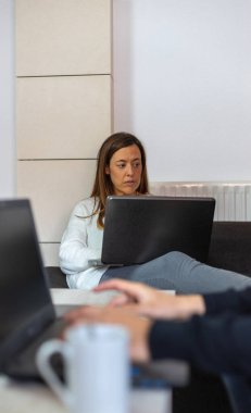 Evde çalışan genç bir çift dizüstü bilgisayarlarıyla kanepede oturuyor.