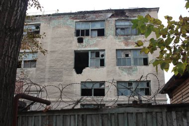 Çitin arkasındaki ön cephesinde kırık camlar olan terk edilmiş bir bina.