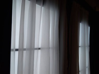 Oturma odasındaki pencerenin iç tarafındaki odada şeffaf beyaz perdeler.
