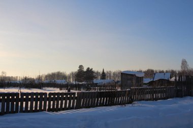 Tahta bir çit köyde kışın bitmemiş bir evi kapatıyor.