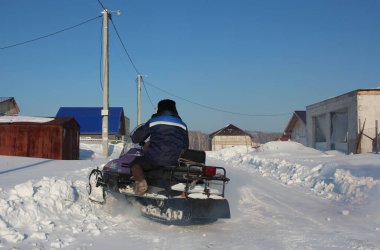 Russia, Novosibirsk 12.02.2021: a man rides a snowmobile in a village in winter in Siberia clipart