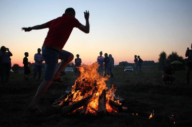 Rusya, Novosibirsk 10.07.2021: bir adam Sibirya 'daki bir gelenek için Pagan bayramında bir şenlik ateşinin üzerinden atlar.