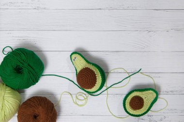 Beyaz ahşap arka planda ipliği olan tığ işi avokado oyuncakları. El işi.