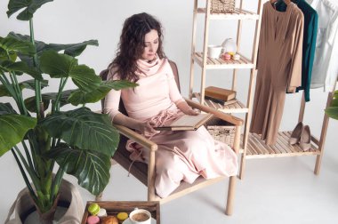 Kıvırcık kadın tahta koltukta oturuyor ve evde kitap okuyor. Açık renkli oturma odası