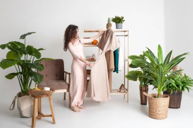 Esmer kadın yeşil bitkiler ve ahşap mobilyalarla oturma odasını seçiyor. Beyaz arkaplan