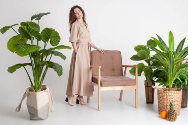 Stüdyoda beyaz arka plan ve yeşil bitkilerle poz veren mutlu esmer kadın.