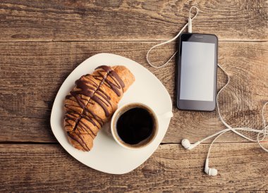 kahve ve kruvasan ile akıllı telefon ve kulaklık
