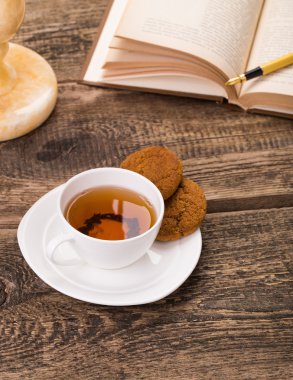 Fildişi çay bardağı tatlı kurabiye, kitap, kalem üzerinde ahşap pa ile görüntü