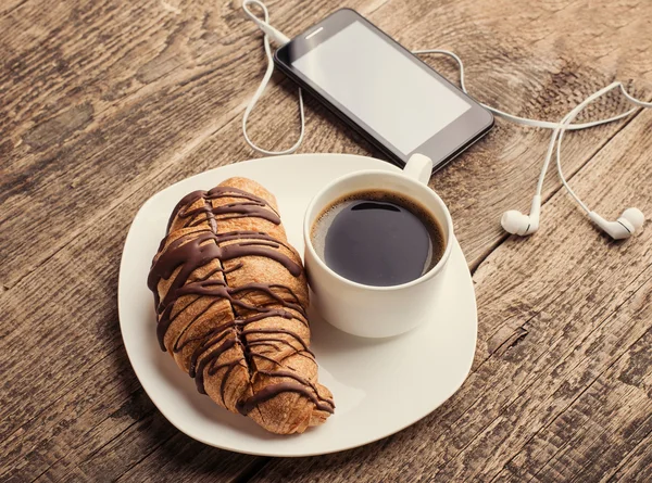 Att ha kaffe och croissanter med smartphone och hörlurar — Stockfoto