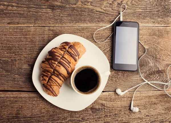 Koffie en croissants met smartphone en hoofdtelefoons — Stockfoto