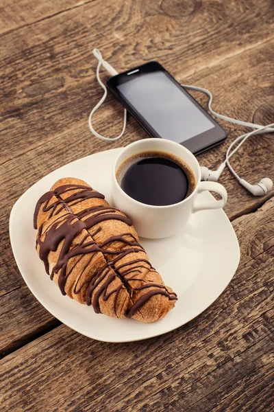 Att ha kaffe och croissanter med smartphone och hörlurar — Stockfoto