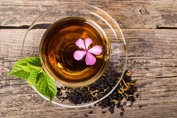Чай из стекла с розовым цветком и мятным листом, на коричневой деревянной па — стоковое фото