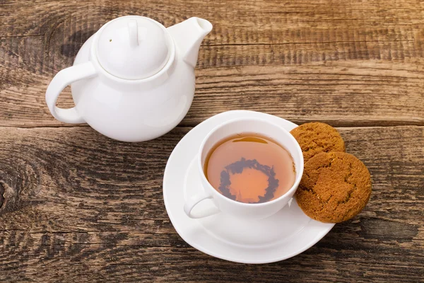 Imagen de la taza de té de marfil con galletas dulces, y hervidor de agua en madera p — Foto de Stock