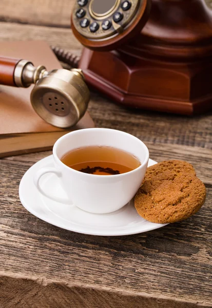 Ivory tea cup with sweet cookie, old telephone and book on woode — Stock Photo, Image