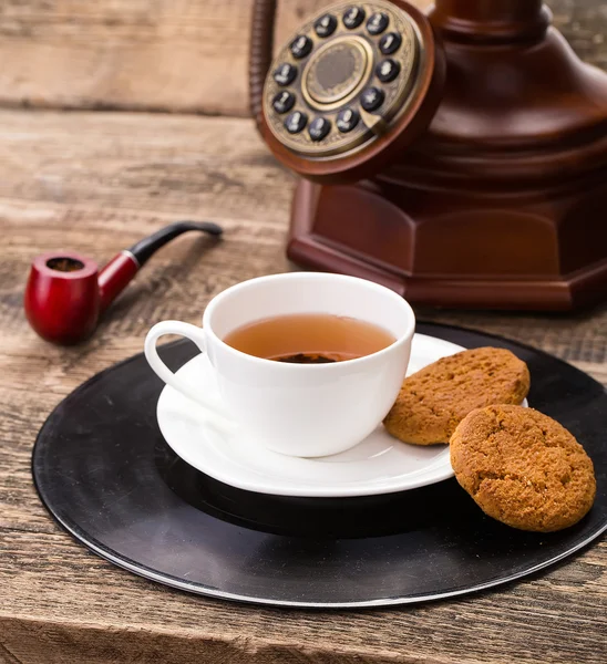 Taza de té de marfil con galletas dulces, teléfono viejo y pipa de tabaco — Foto de Stock