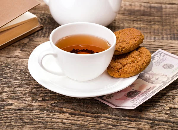 Ivory tea cup with sweet cookie, and dollar money on wooden pale — Stock Photo, Image