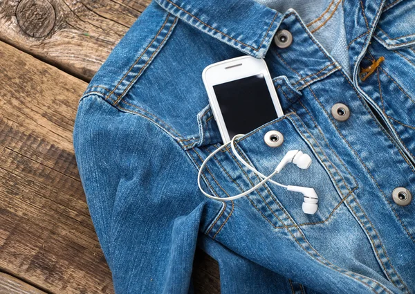 Hörlurar och smartphone i pocket gammal jeansjacka — Stockfoto