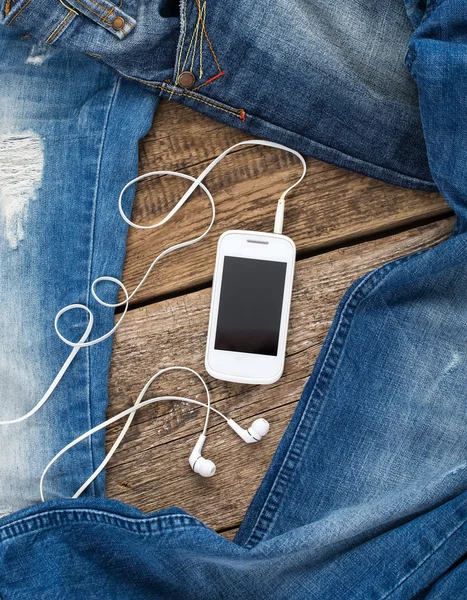 Jeans around mobile smartphone with earphones on old wooben back — Stock Photo, Image