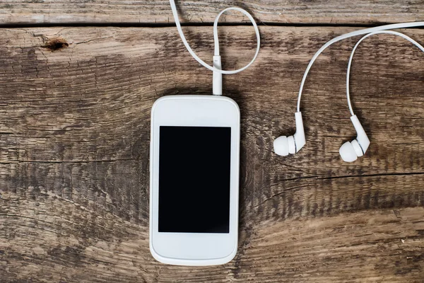 Weißes Smartphone mit Kopfhörer und isoliertem Bildschirm auf altem Holz — Stockfoto