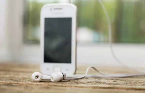 Kulaklık ve eski ahşap izole ekranda beyaz akıllı telefon — Stok fotoğraf