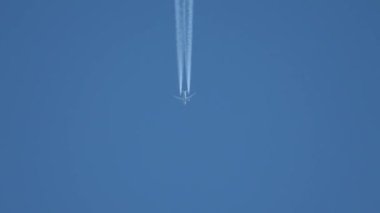 Gökyüzünde yükseklerde uçan jet uçağı açık mavi gökyüzünde kontrastlar bırakır.
