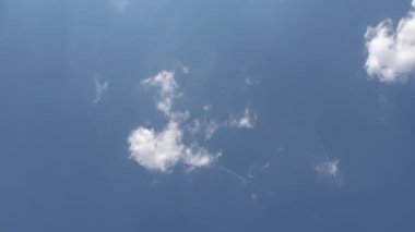 Mavi gökyüzünde buhar izi olan bir uçak bulutlara doğru uçuyor.