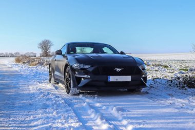 Güneşli bir günde Almanya 'da bir kış manzarasının önündeki siyah Ford Mustand spor arabası