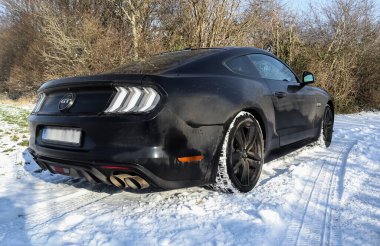 Güneşli bir günde Almanya 'da bir kış manzarasının önündeki siyah Ford Mustand spor arabası