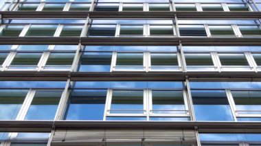 Bir ofis binasının cam cephesinden yansıyan bulutlarla dolu mavi bir gökyüzünün zaman akışı..