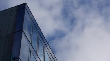Bir ofis binasının cam cephesinden yansıyan bulutlarla dolu mavi bir gökyüzünün zaman akışı..