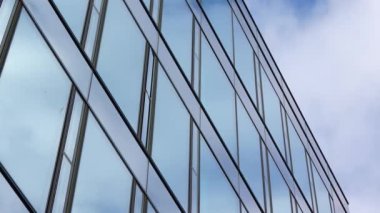 Bir ofis binasının cam cephesinden yansıyan bulutlarla dolu mavi bir gökyüzünün zaman akışı..