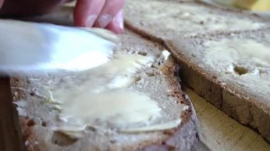 Tahta bir tabakta taze bir ekmek dilimine tereyağı sürüyorum.
