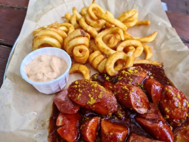 Geleneksel Alman körili sosisi, beyaz tabakta cips ile servis edilir. Arkaplan olarak tahta tablo.