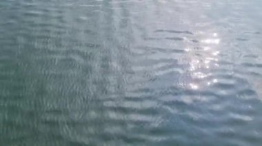 Su yüzeyinin detaylı yakın görüntüsü dalgalar, dalgalar ve güneş ışığı yüzeye yansıyor.