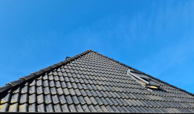 Siyah çatı kiremitleri ve mavi gökyüzü arkaplanı olan velux tarzı bir çatı penceresi aç