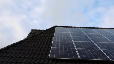 Newly installed photovoltaic solar panels on a house roof. Blue sky with clouds reflecting on the modules creating a clean energy source
