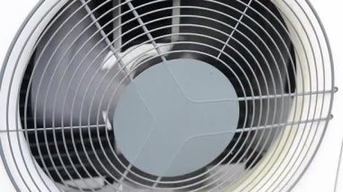 Close up view of the external unit of an air conditioner or heat pump. The fan blades rotate slowly, cooling the compressor