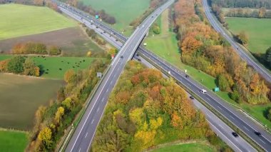 Cars and trucks driving through a complex highway interchange in the german countryside surrounded by colorful autumn forests and green fields
