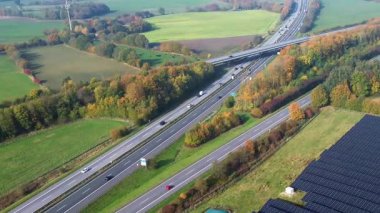 Aerial view of the A7 highway near Hamburg, Germany. Cars and trucks driving through a rural landscape with a solar panel farm