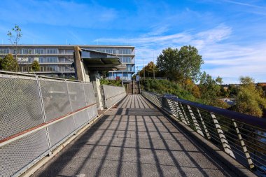 Kiel, Almanya - 17. Ekim 2025: Mavi gökyüzü altında çağdaş bir binaya uzanan çarpıcı gölgeli yaya köprüsü