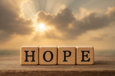 Umut kelimesini oluşturan dört tahta küp, bulutlarla dolu günbatımı gökyüzünün sıcacık parıltısıyla aydınlanan ahşap bir masanın üzerinde duruyor.